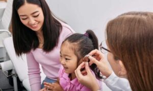 An audiologist fits a young girl with a hearing aid