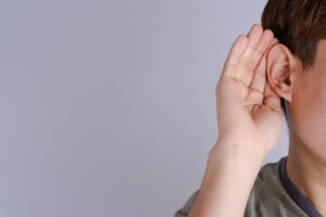 Picture of a young man putting his hand to his ear, indicating that he has difficulty hearing and needs aural rehabilitation.